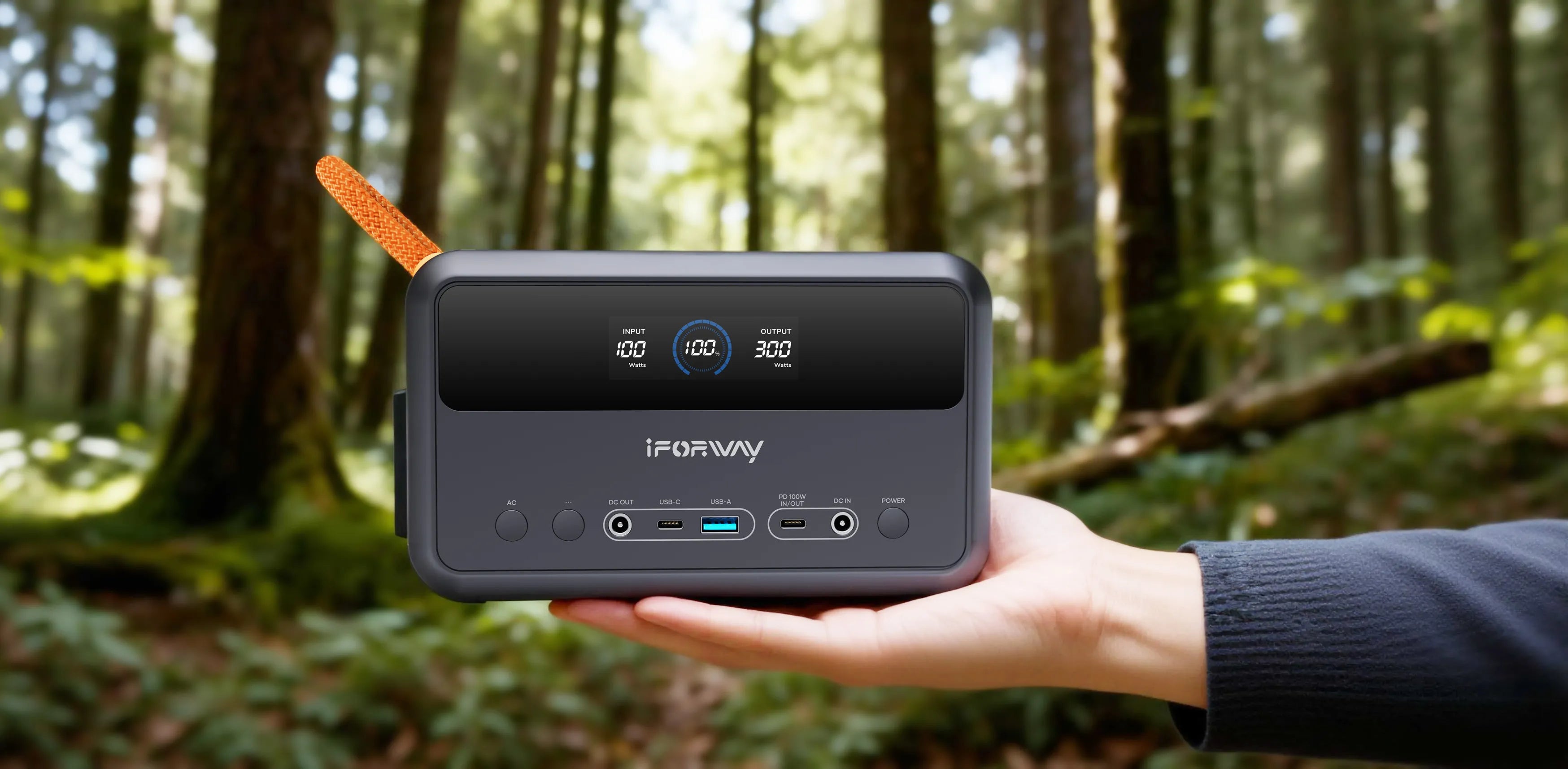 A handheld demonstration of the iFORWAY 300W portable power station against a lush forest backdrop. Highlighting its ultra-compact and portable design that fits easily into backpacks for on-the-go energy. Featuring a 300W high power output and PD 100W bidirectional fast charging, this lightweight unit with an orange carry handle is the perfect reliable companion for hiking, trekking, and wilderness exploration.