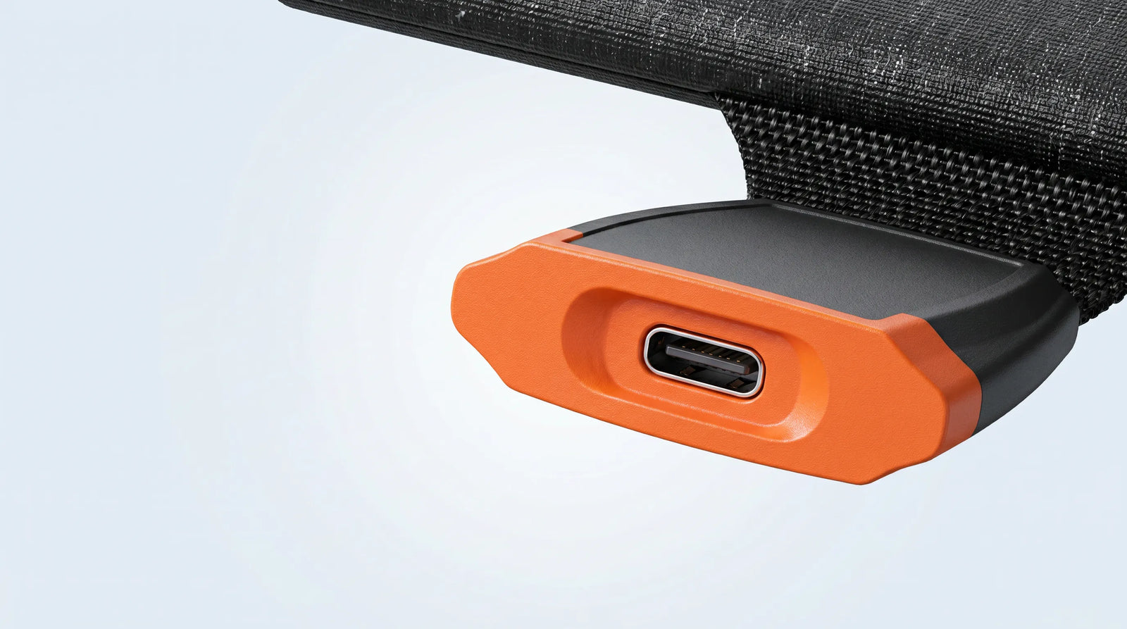 A detailed, macro-style close-up of the integrated USB-C output port module on the iFORWAY 36W Backpacking Solar Charger. The image focuses on a single USB-C port, clearly displaying its precise oval shape and internal connector. The port is framed by a distinctive, durable orange plastic housing with a textured surface for easy handling. This housing is securely fastened to the heavy-duty black fabric of the solar panel, which shows a small integrated fabric loop, emphasizing the charger's portable and adv