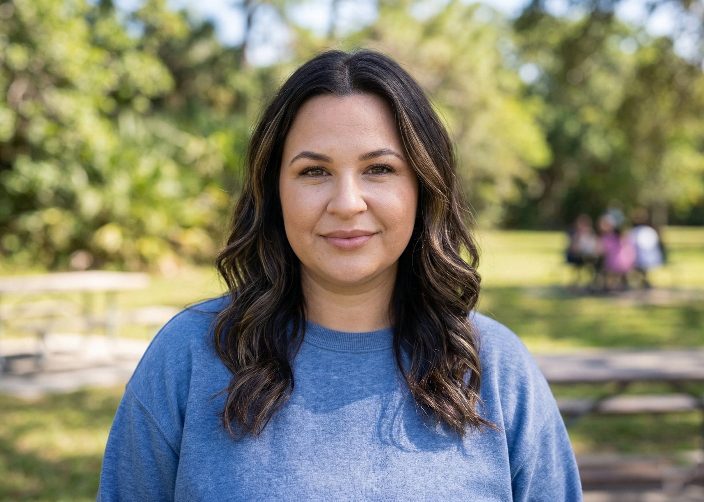 A friendly, smiling woman in a sunny park setting. As a loyal user of iFORWAY 300W portable power stations, she embodies the stress-free lifestyle of having reliable power for mobile devices during family weekend picnics and outdoor leisure activities.