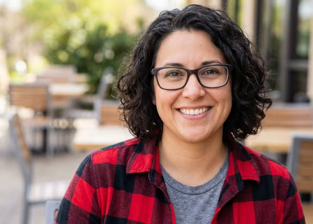 A smiling woman with glasses and a plaid shirt sitting outdoors. Representing a satisfied customer of iFORWAY portable power stations, she highlights our community of remote workers and outdoor enthusiasts